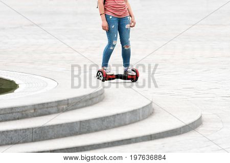 Young woman riding a hoverboard on the city square. New movement and transport technologies. Close up of dual wheel self balancing electric skateboard. People on electrical scooter outdoors