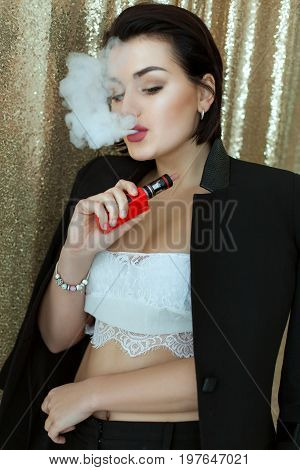 Beautiful woman is vaping. She exhales steam from an electronic cigarette.