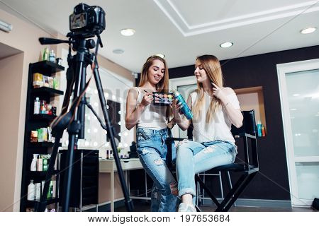Smiling female beauty bloggers reviewing make-up products for their blog recording a video on camera in salon.
