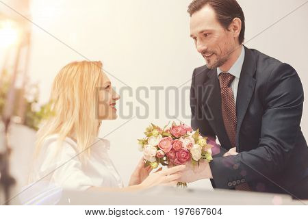 Pleasant gesture. Handsome attentive friendly gentleman presenting a bouquet and wishing a leady all the best while she celebrating her birthday at work