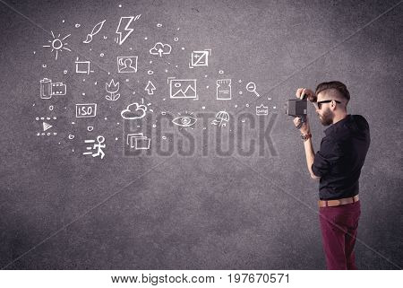 An elegant hipster guy trying to use a vintage camera with camera settings icons drawn on wall, like flash, white balace or ISO value concept