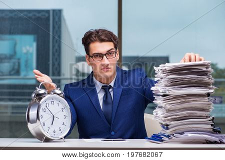 Businessman with pile stack of paper paperwork and an alarm cloc