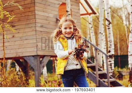 happy child girl playing little gardener in autumn and picking leaves into basket. Seasonal garden work.