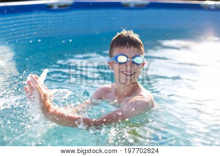 Happy kid with teeth smile splasing in swimming pool enjoying summer holiday