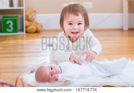Happy toddler girl playing with her newborn baby sister
