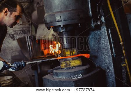 The blacksmith manually forging the molten metal on the anvil in smithy with spark fireworks