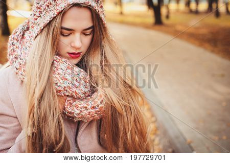 portrait of young beautiful woman walking in stylish warm outfit in sunny autumn day in park wearing pink coat and knitted snood. Casual lifestyle in the city