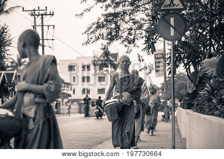 LUANG PRABANG LAOS - MARCH 12 2017: Black and white horizontal picture of young monks going in line to Buddhist Alms Giving Ceremony where local people offers food and money before the sunrise in Luang Prabang Laos.