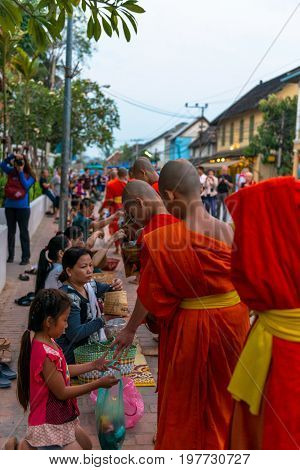 LUANG PRABANG LAOS - MARCH 12 2017: Vertical and from the back picture of monks receving food and money at Buddhist Alms Giving Ceremony before the sunrise in Luang Prabang Laos.