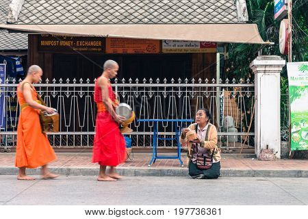 LUANG PRABANG LAOS - MARCH 12 2017: Lao woman on her knees waiting the monks come to give them food and money for the Buddhist Alms Giving Ceremony before the sunrise in Luang Prabang Laos.