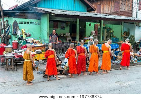 LUANG PRABANG LAOS - MARCH 12 2017: Wide angle picture of local people giving food and money to the monks for the Buddhist Alms Giving Ceremony in Luang Prabang Laos.