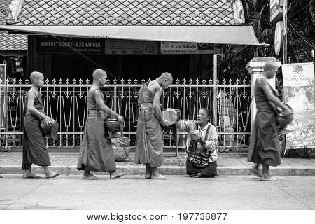 LUANG PRABANG LAOS - MARCH 12 2017: Black and white picture of Lao woman on her knees giving to the monks food and money for the Buddhist Alms Giving Ceremony before the sunrise in Luang Prabang Laos.