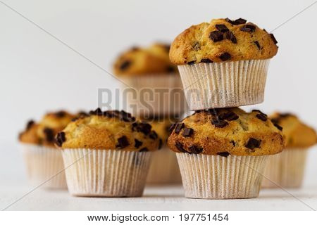 Many tasty homemade vanilla muffins with chocolate chunks on bright white background. Closeup.