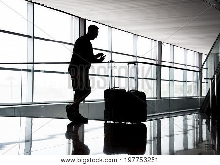 Sillouhette of a man with luggage and cell phone at the airport