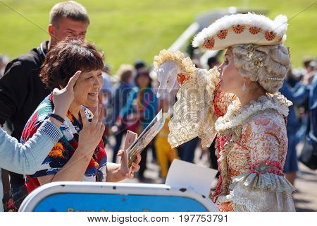 PETERHOF/ RUSSIA - JULY1, 2017. Asian tourists want to be photographed with the model in an ancient court costume in the Peterhof park. Saint Peterbug, Russia.