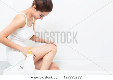 Young beautiful woman applying body lotion on her attractive legs in bathroom.
