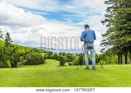 Landscape view of green golf course with hills in summer in La Malbaie Quebec Canada in Charlevoix region with photographer and tripod