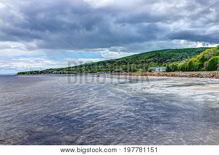 La Malbaie Canada - June 2 2017: Saint Lawrence river shore stormy waves and clouds with cityscape skyline and road of town village