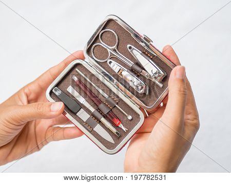 Closeup woman hand holding traveler's nail care kit of necessary tools set including scissors tweezers nail file and trimmer in red leather pocket case.