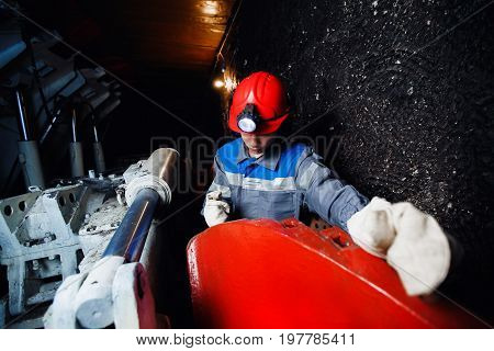 young miner man underground in a mine for coal mining in overalls is busy with work, repairing against the backdrop of mining equipment. Portrait.