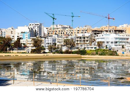 BUGIBBA, MALTA - MARCH 31, 2017 - View of salt pans with buildings and construction cranes to the rear in Salina Bay Bugibba Malta Europe, March 31, 2017.