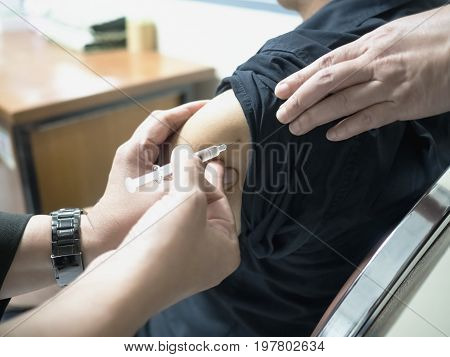 Close up of patient getting a vaccination in the hospital. The injection are treated by a nurse on the patient's upper arm with sterile equipment.