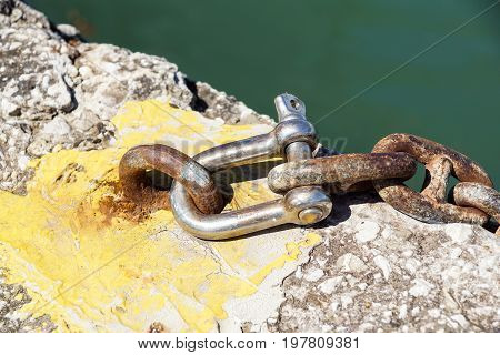 Rusty metal shackle on a metal bar laying on weathered wood outdoors