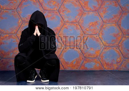Young dancer wearing hood sitting near the wall. Urban style