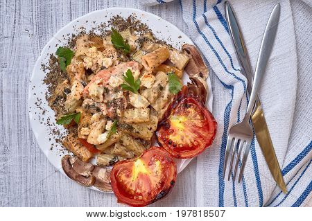 Paste from macaroni with vegetables, with tomatoes and seasoned with a basil. It is decorated with parsley. On a light background with ordinary devices.