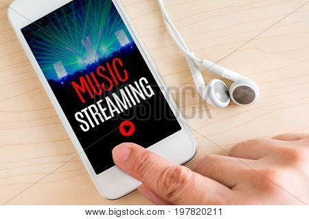 Hand touch smart phone and ear phone with Music Streaming word on wood table Internet marketing concept