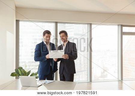 Two serious businessmen discussing building plan, investment adviser offering new project to investor, partners considering construction investment, joint venture business, buying real estate