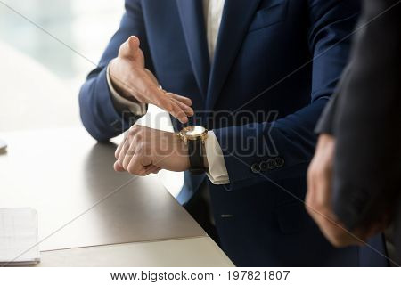 Close up view of businessman wearing suit pointing on hand expensive luxury wristwatch at meeting, showing unpunctual partner he is being late, punctuality management concept, time is money