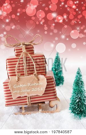 Vertical Image Of Sleigh Or Sled With Christmas Gifts Or Presents, Snow And Trees. Red Sparkling Background With Bokeh. Label With German Text Guten Rutsch Ins Jahr 2018 Means Happy New Year