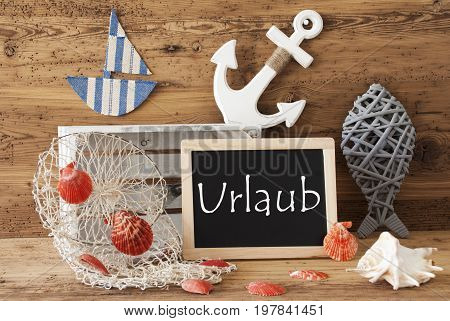 Blackboard With Nautical Summer Decoration And Wooden Background. German Text Urlaub Means Holiday. Fish, Anchor, Shells And Fishnet For Maritime Contex.