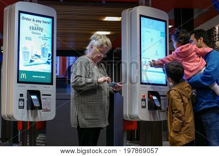 Coquitlam, BC, Canada - April 11, 2017 : Family ordering food at self check out machine and old lady playing cellphone at Mcdonalds restaurant