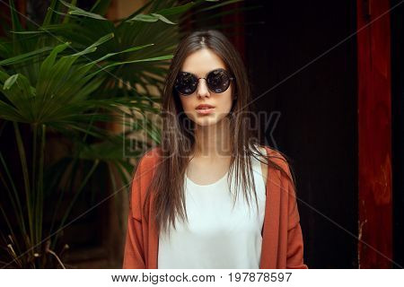 people emotions natural beauty and lifestyle concept - close up portrait young girl in white shirt jeans and sunglasses vintage fashion style around the palm trees . Summer beauty concept