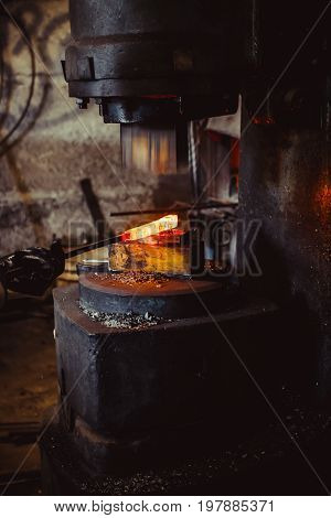 The blacksmith manually forging the molten metal on the anvil in smithy with spark fireworks
