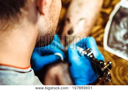 Russia Novokuzneck 5.07.2017: The tattoo artist makes a tattoo on the client's neck in the tattoo salon. The master does a tattoo in the studio. Close-up. Hard. Pain.