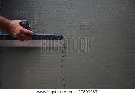 Hands Of An Old Manual Worker With Wall Plastering Tools Renovating House. Plasterer Renovating Outd
