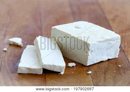 Single Block Of White Tofu And Two Tofu Slices With Crumbs On Wooden Chopping Board.