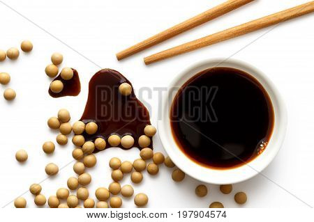 Soya Sauce In White Ceramic Bowl On White From Above With Wooden Chopsticks. Spilled Soya Sauce And