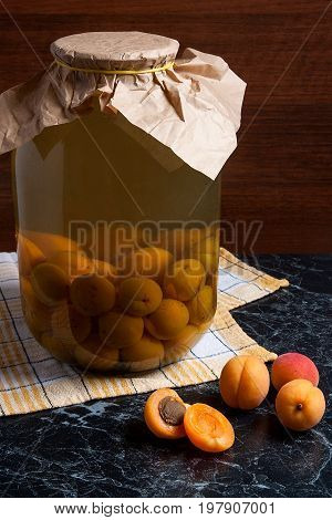 Juicy Harvested Apricots And Big Glass Jar With Canned Apricot Compote On Dark Marble..