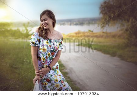 Half length portrait of charming positive woman dressed in long white summer dress happy smiling in sunset background. Beautiful woman enjoying free time.