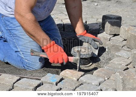 Photo of stonemason who is repairing cobblestone road.