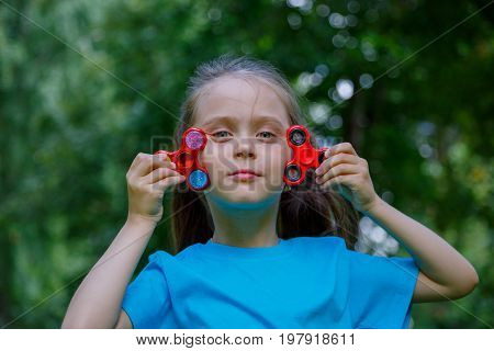 Cute school girl playing with colorful fidget spinner in outdoor. Popular stress-relieving toy for school kids and adults.
