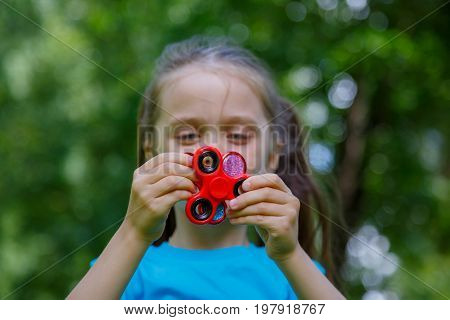 Little girl playing with fidget spinner. Child spinning spinner in park. Blurred background.