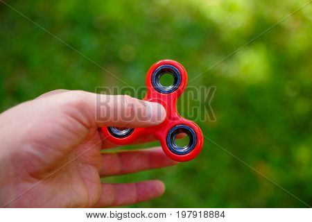 Closeup of a young caucasian man playing with red fidget spinner on f the soccer artificial field. Popular spinner gadget