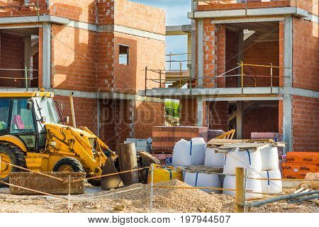 Construction site red brick residential townhouses concrete pillars digger piles of materials unfinished new build. Spain, Torrevieja, August 2017