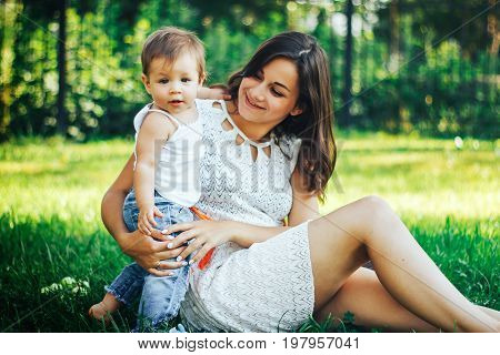Young beautiful mother sitting with her child on a green grass and playing together
