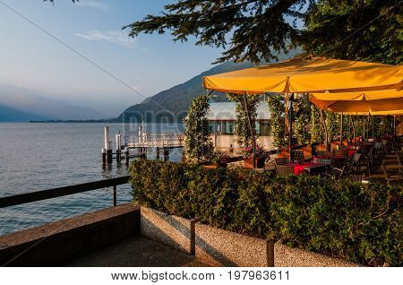June 13th, 2017 - Lombardy, Italy. Waterfront restaurant in Bellano fishing village, situated on Como Lake shore. Cafe tables, lake and mountains view by sunset in small coast town Bellano.